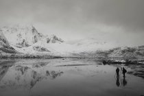 Photographers below snow covered mountains and calm bay, Norway — Stock Photo