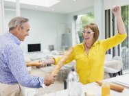 Playful mature couple sword fighting with baguettes in kitchen — Stock Photo