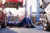 Mecánico debajo del coche en taller de reparación de automóviles - foto de stock