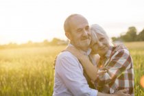 Cariñosa y serena pareja de ancianos abrazándose en el soleado campo de trigo rural - foto de stock