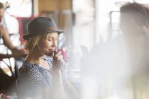 Femme au chapeau buvant du café au café — Photo de stock