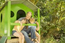 Padre e hijos relajándose juntos en la casa del árbol - foto de stock