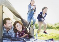 Smiling couple in tent watching kids running in grass — Stock Photo