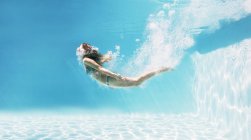 Mujer nadando bajo el agua en la piscina - foto de stock