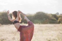 Boho woman in king dancer yoga pose in sunny rural field — Stock Photo