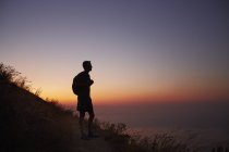 Silhueta de caminhante masculino em trilha com vista para o oceano ao pôr do sol — Fotografia de Stock
