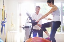 Physical therapist guiding woman on stationary bike — Stock Photo