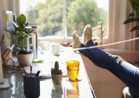 Жінка розмовляє по телефону з ногами вгору на столі в сонячному домашньому офісі — стокове фото