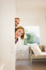 Portrait playful mature couple peering from behind door — Stock Photo