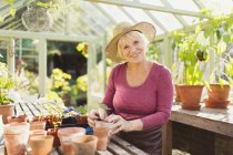 Portrait smiling senior woman potting plants in greenhouse — Stock Photo