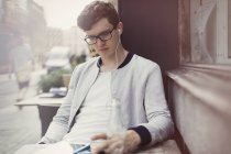 Молодий чоловік з окулярами та навушниками використовує цифровий планшет у тротуарному кафе — стокове фото