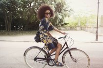 Retrato sorridente mulher com afro andar de bicicleta no parque urbano — Fotografia de Stock