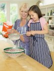 Grandmother and granddaughter baking sifting flour in kitchen — Stock Photo