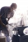 Herrero moldeando hierro sobre yunque en forja - foto de stock