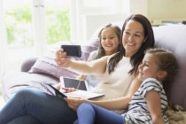 Mother and daughters taking selfie on living room sofa — Stock Photo