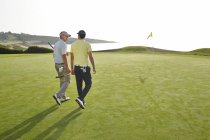 Чоловіки йдуть до діри на полі для гольфу з видом на океан — стокове фото