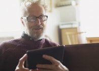 Hombre mayor con anteojos usando tableta digital - foto de stock