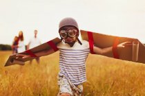 Boy with wings in aviators cap and flying goggles in field — Stock Photo