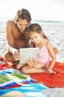 Батько і дочка використовують цифровий планшет на пляжі — стокове фото