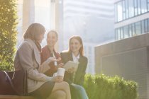Mujeres de negocios sonrientes con tableta digital bebiendo café al aire libre - foto de stock