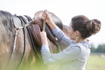 Woman tightening horse saddle for horseback riding — Stock Photo