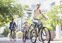 Mother and son in helmets riding tandem bicycle in urban park — Stock Photo