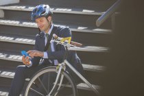 Empresário de terno com bicicleta e capacete SMS com telefone celular nas escadas — Fotografia de Stock