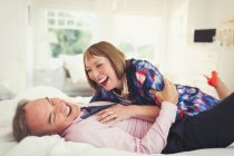 Well-dressed mature couple laughing on bed — Stock Photo