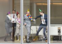 Gente de negocios juguetona en sombreros de fiesta bailando en la ventana de la sala de conferencias - foto de stock