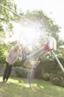 Grandmother pushing carefree granddaughter on swing in backyard — Stock Photo
