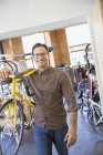 Retrato sorridente homem com óculos transportando bicicleta na loja de bicicletas — Fotografia de Stock