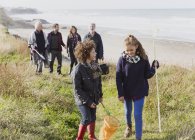 Familia multigeneracional con redes que caminan por sendero de playa de hierba soleada - foto de stock