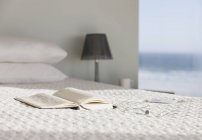 Книга и очки на кровати в современной спальне с видом на океан — стоковое фото