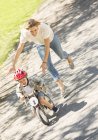 Mãe empurrando filho com capacete na bicicleta no parque ensolarado — Fotografia de Stock