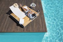 Man relaxing on lounge chair at poolside with tablet — Stock Photo