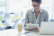 Femme d'affaires souriante utilisant une tablette numérique avec du café au bureau — Photo de stock