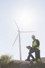 Worker using laptop by wind turbine in rural landscape — Stock Photo