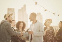 Молоді дорослі друзі рукостискають на вечірці на даху — стокове фото