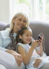 Бабуся і онука діляться навушниками, слухаючи музику на дивані — стокове фото