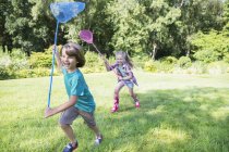 Junge und Mädchen rennen mit Schmetterlingsnetzen im Gras — Stockfoto