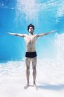 Mann steht mit ausgestreckten Armen unter Wasser in Schwimmbad — Stockfoto