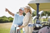 Senior couple standing next to golf cart — Stock Photo