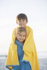Frère et sœur enveloppés dans des serviettes sur la plage — Photo de stock