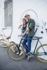 Portrait smiling couple with bicycles hugging at urban wall — Stock Photo