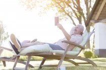 Homem sênior usando tablet digital relaxante na cadeira lounge no quintal — Fotografia de Stock