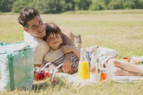 Portrait affectionate father and son relaxing on picnic blanket in sunny field — Stock Photo