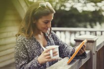 Жінка п'є каву і використовує цифровий планшет на балконі — стокове фото