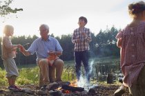 Grandfather and grandchildren enjoying campfire at lakeside — Stock Photo