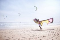 Homem correndo com kiteboarding pipa na praia ensolarada — Fotografia de Stock