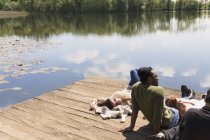 Friends laying relaxing on sunny lakeside dock — Stock Photo
